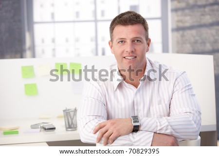 Male casual office worker smiling in office, sitting.?