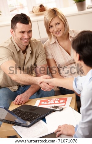 Estate agent shaking hand with young man, making deal with smiling couple in new house.?