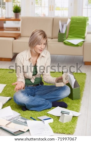 Woman checking documents and credit card account, shocked by financial situation, sitting at home on floor.?