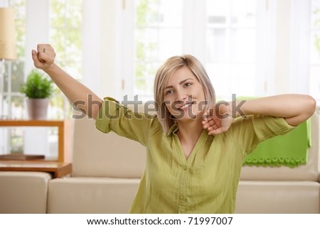 Smiling mid-adult woman stretching in front of sofa in bright living room.?