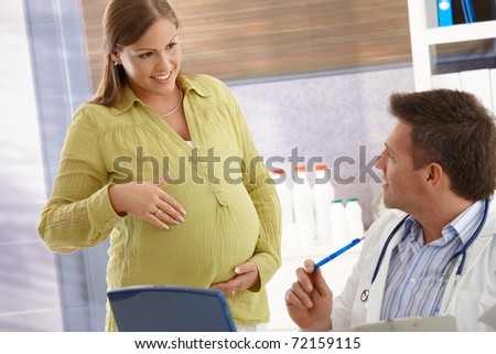 Expectant woman pointing at tummy, smiling at doctor in consulting room.?
