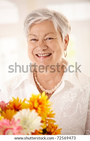 Closeup portrait of happy elderly woman holding flowers looking at camera, smiling.?