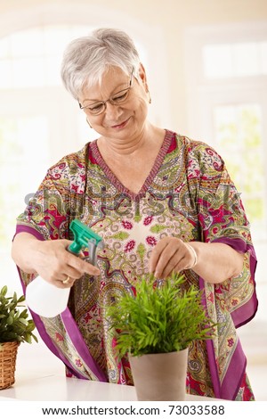 Happy elderly woman watering plant at home, smiling.?