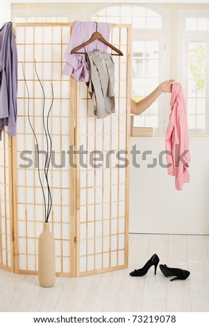 Woman undressing behind dressing panel, holding out pink shirt.?