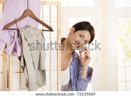 Happy young woman talking on mobile while dressing up, smiling.?