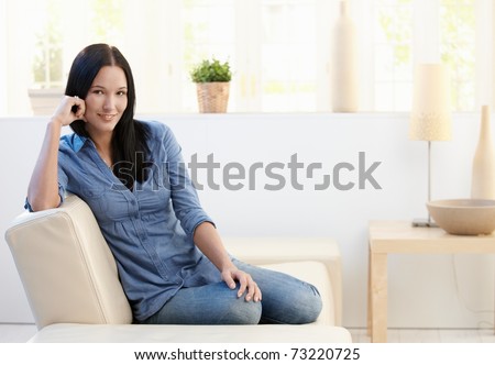 Portrait of attractive young woman sitting on couch at home, looking at camera, smiling.?