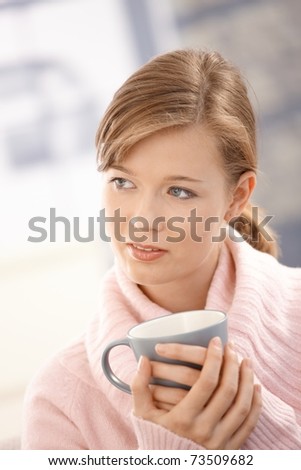 Closeup portrait of young woman wearing pullover, holding tea mug.