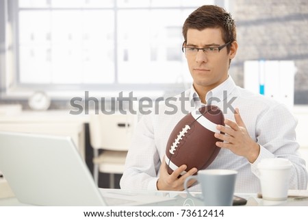Troubled businessman thinking about work playing with football handheld in office.?