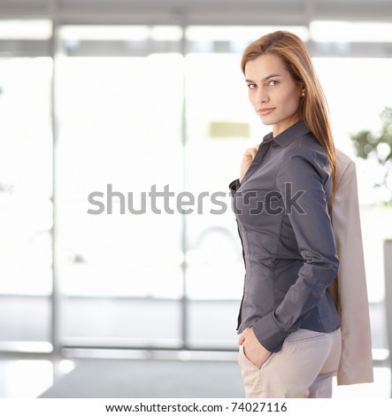 Young businesswoman leaving office, looking back at camera, smiling. Copy space on left.?