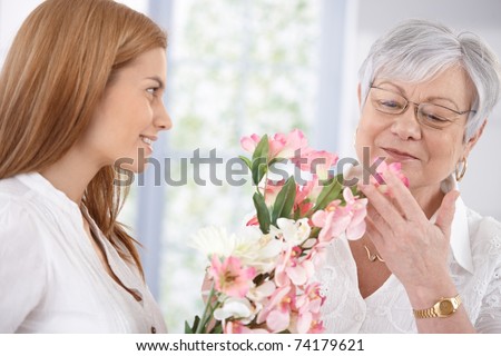 Pretty woman greeting her mother at mother\'s day, giving flowers, both smiling.?