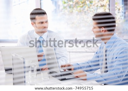 Young businessman working in bright office behind blind.?