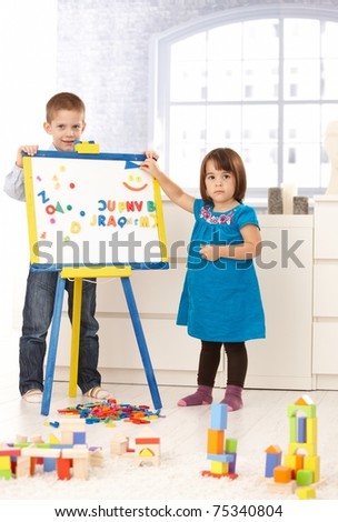 Portrait of creative small kids standing at drawing board, playing with alphabet.?