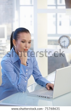 Smart businesswoman working on laptop computer, looking at screen, smiling.