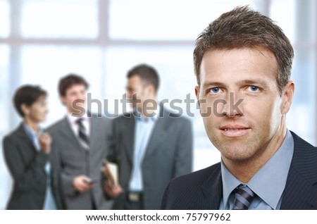Closeup businessman portrait in office, cheerful colleagues in background.?