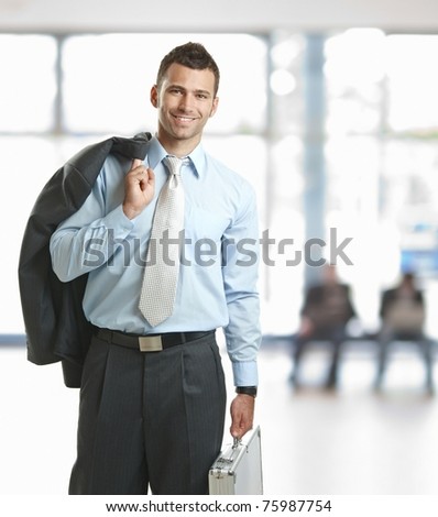 Smiling businessman standing in lobby with suitcase, leaving office.?
