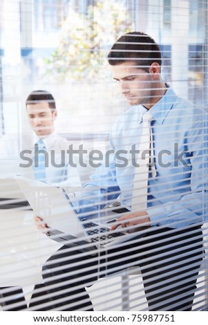 Young businessman working in modern office behind blind.?