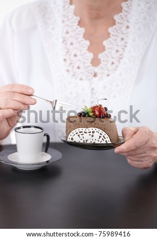 Woman sitting at coffee table having coffee and cake face is not visible.?