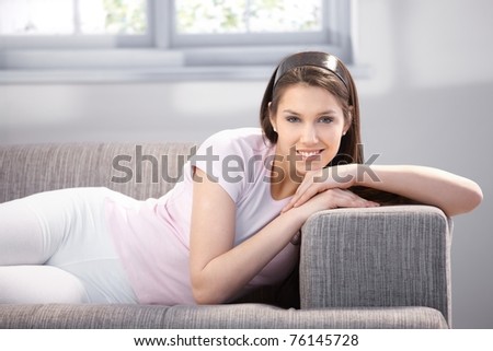 Pretty young girl laying on sofa, smiling, looking at camera.?