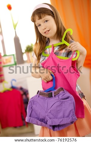 Portrait of small girl presenting combination of clothes on hanger, smiling.?