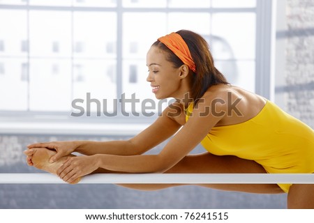 Cheerful ballerina bending at training, stretching at ballet bar, smiling.?