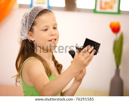 Portrait of small girl using makeup, looking at pocket mirror.?