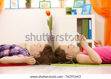 Schoolgirls listening to music via headset on mp3 player together, smiling, lying on floor.?