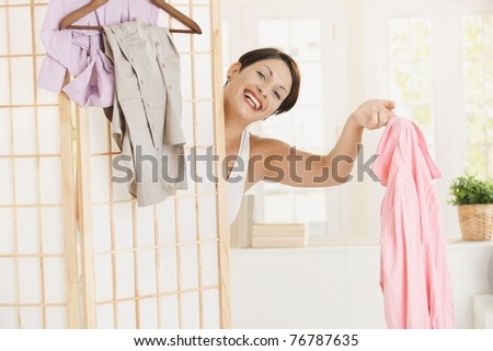 Happy young woman dressing up, looking out behind dressing panel, showing up pink shirt.?