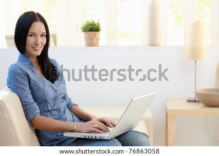 Portrait of young woman sitting at home with laptop computer, smiling at camera.?