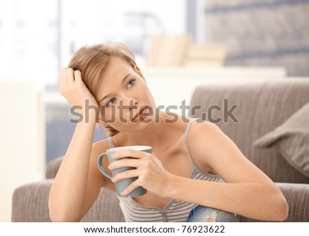 Troubled woman sitting on floor at home, thinking with tea in hand.?