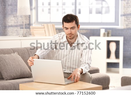 Young man browsing Internet at home, sitting on sofa, looking at screen.?