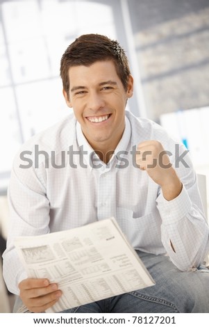 Portrait of man happy about news, smiling at camera, holding newspaper.?