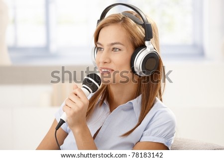 Attractive young woman singing with microphone, wearing headphones, smiling.?