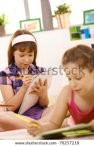 Schoolgirls writing homework together, using exercise books at home.
