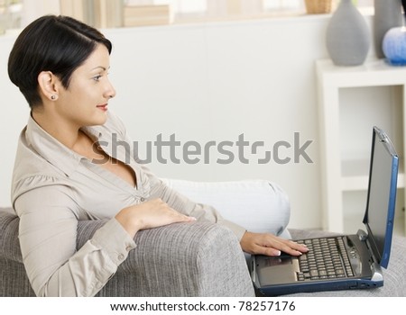Young woman sitting on sofa at home, using wireless network with laptop.
