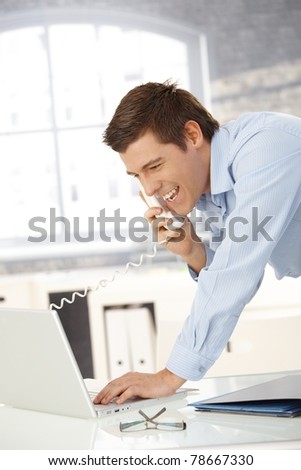 Laughing professional man on landline call with laptop computer, looking at screen.?