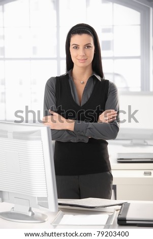 Portrait of smart office girl standing at desk with arms folded, smiling.?
