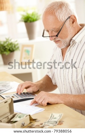 Older man concentrating on financial job, using calculator at home.?