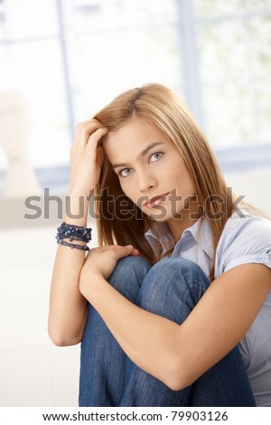Attractive woman sitting on floor front of window, hugging knees.?