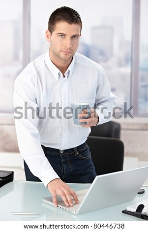 Young male casual office worker using laptop in bright office.?