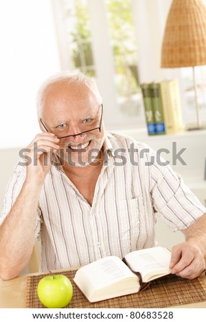 Portrait of laughing senior looking at camera, sitting with book at table.