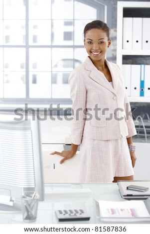 Happy office worker girl posing at desk, smiling at camera.?