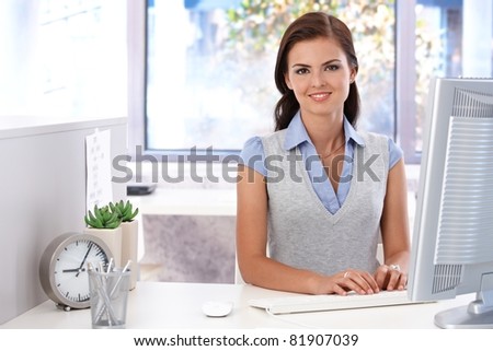 Attractive young girl using computer in bright office, smiling.?