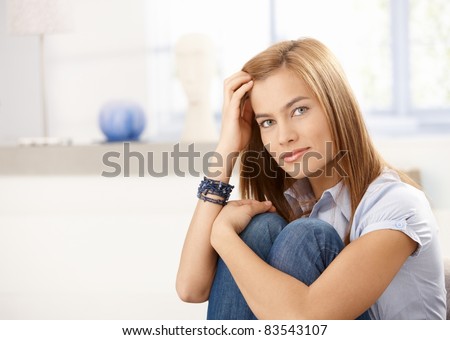 Attractive woman sitting on floor front of window, hugging knees, smiling.?