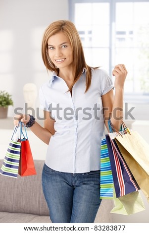 Young attractive woman standing in living room with shopping bags, smiling.?