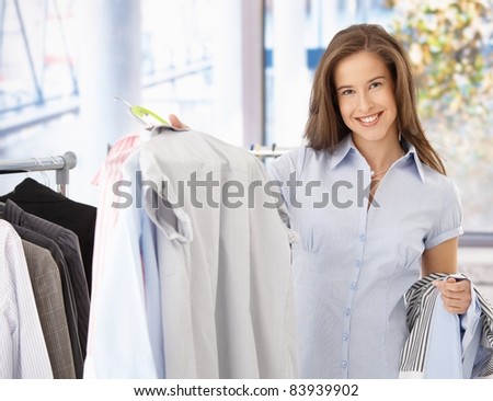 Happy female customer in clothes shop, holding shirt, smiling at camera.?