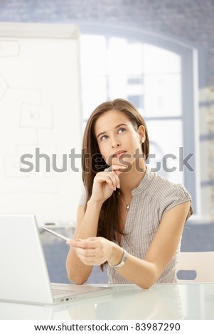 Businesswoman thinking at desk, using laptop computer, concentrating, looking up .?