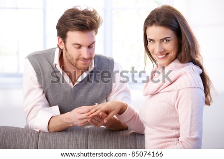 Attractive young couple having engagement, man pulling engagement ring on womans finger, smiling.?