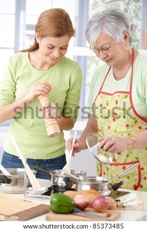 Senior mother and young daughter preparing food in kitchen, having fun, smiling.?
