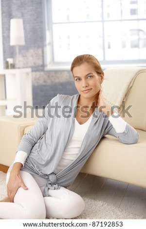 Portrait of pretty woman sitting on floor, posing in front of sofa in living room, smiling at camera.?