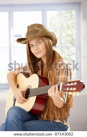 Attractive young girl playing guitar in western hat.?